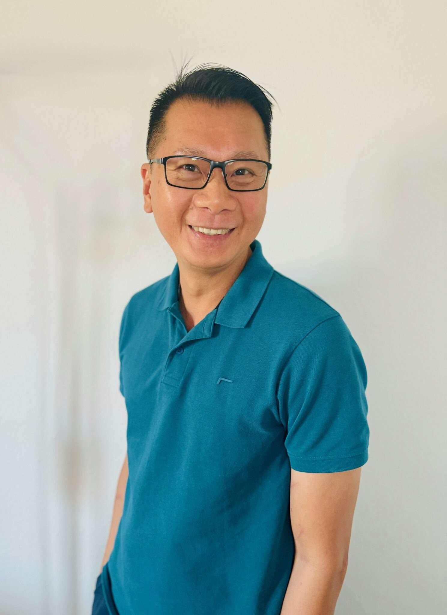 Krish Phua smiling, wearing glasses and a teal shirt