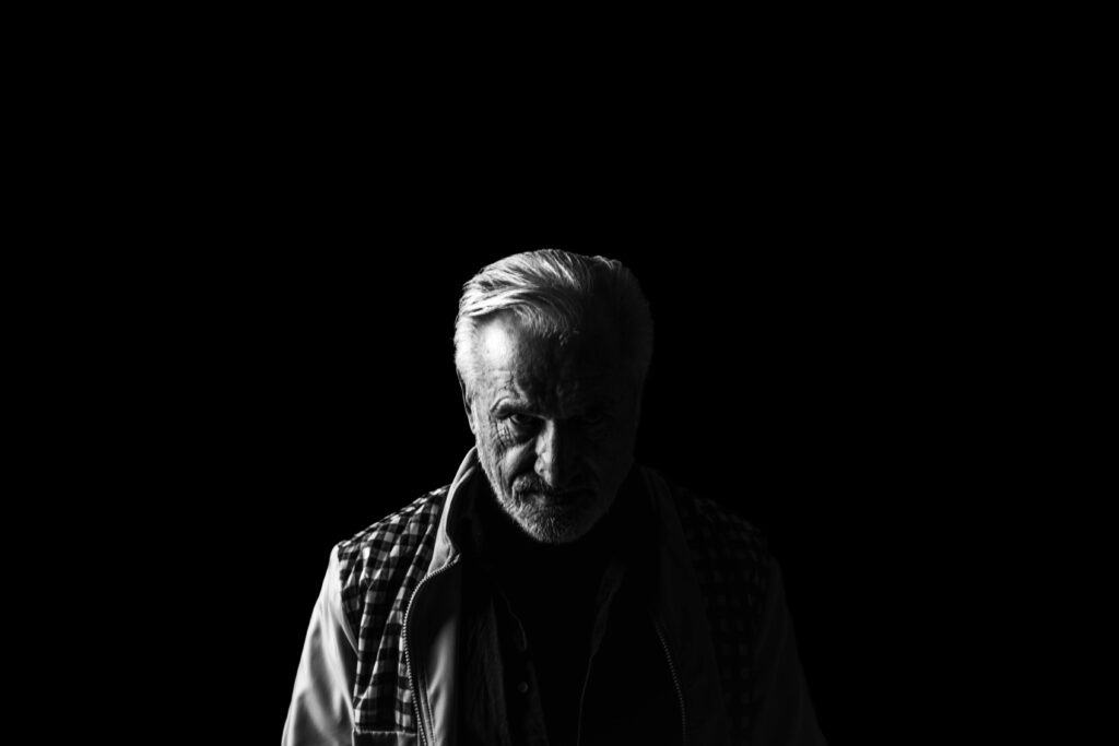 old man with lowered head in the dark symbolising midlife crisis