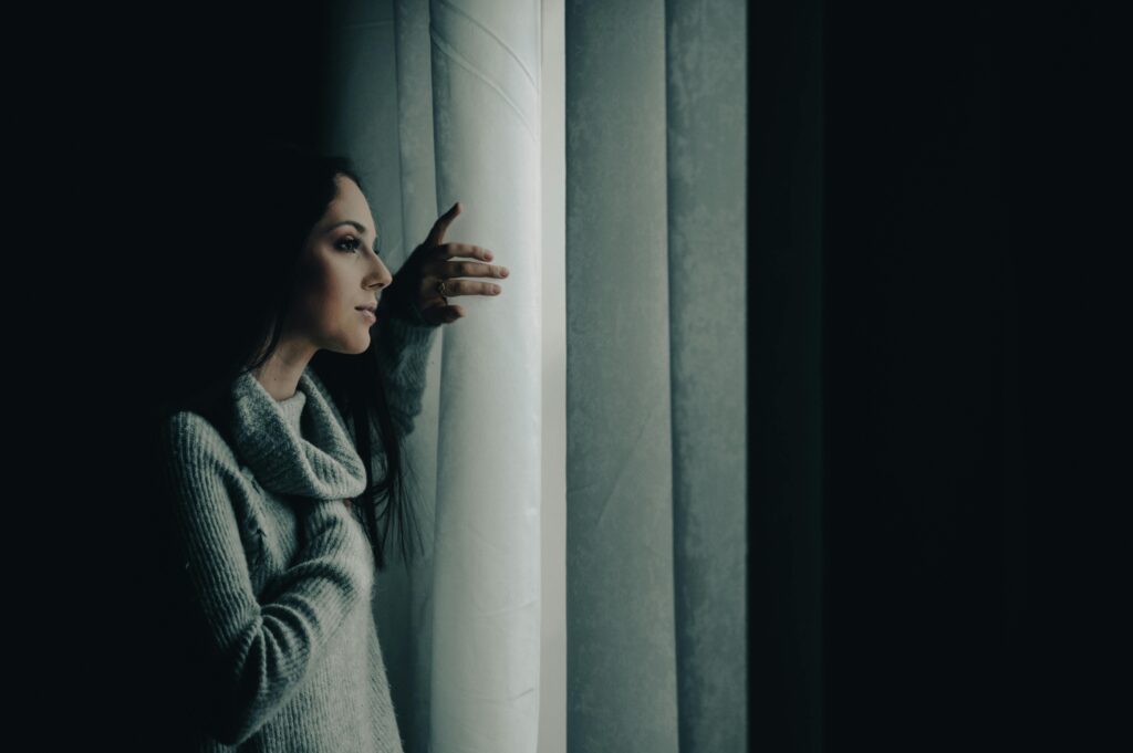 woman in the dark looking out of the window and holding back the curtains symbolising sleep problems and restlessness