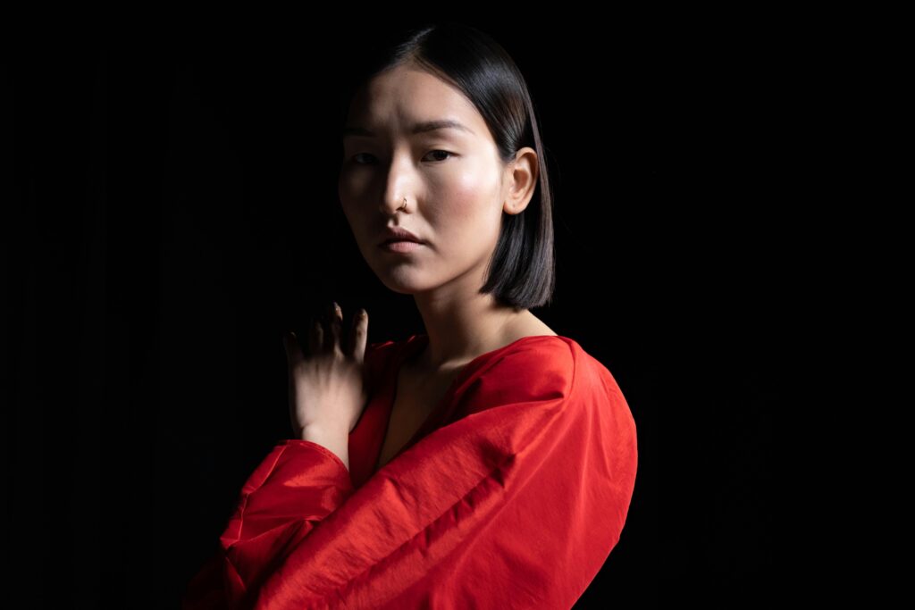 Asian woman in a red dress in the dark with a serious and sad facial expression symbolising coping with trauma, separation or loss